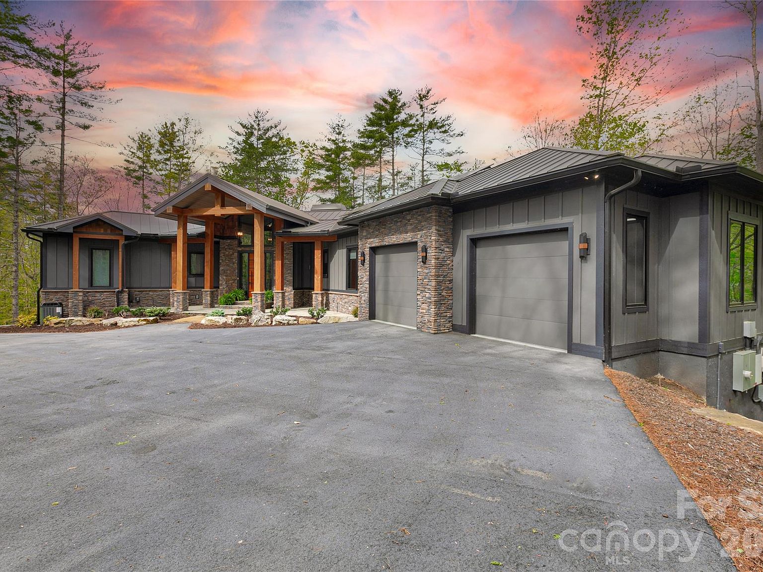 726 Ugugu Drive at twilight. A modern mountain estate of stone, board-and-batten, and timber, set under a soft pink Blue Ridge sky, with a quiet driveway bending into the trees.